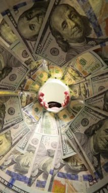 Dikey video. Yüz Dolarlık banknotlarla dolu bir kavanozun içinden bir adamın geniş gözlü bir ifadeyle içeriye bakması dramatik ve ilginç bir atmosfer yaratıyor. Zenginlik Gözlemine Odaklan