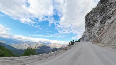 Uçurumun kenarındaki kirli yol geniş bir vadi ve uzak sıradağların panoramik manzarasıyla dağınık bulutlarla kaplı açık mavi bir gökyüzünün altında. Cliffside Sürücüsü