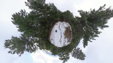 Küçük gezegen etkisi, uzun çam ağaçlarıyla çevrili karla kaplı bir orman patikasında yürüyen birini gösteriyor. Dairesel, gerçeküstü bir perspektif yaratıyor. Kapalı Kış Yolu