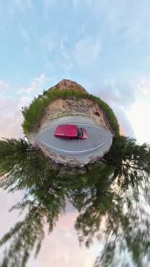 Dikey video. Kıvrımlı Dağ Yolu 'ndaki Kırmızı Araba Hava Görüntüsü Küçük Gezegen Efekti' nde, Rocky Arazisi ve Gökyüzü Altındaki Çam Ağaçları tarafından çevrelendi. Eşsiz Macera Sürücüsü