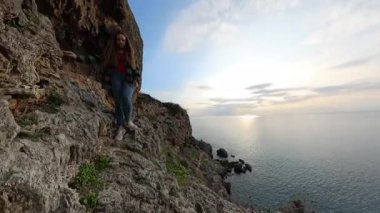 Gün batımında Dar Kayalık Yol boyunca Tek Başına Yürüyen Bir Kadın, Okyanus ve Bulutların Ufuk 'a uzandığı Deniz' e doğru. Manzaralı Yalnız Yürüyüş