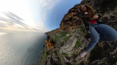 Bir Kadın ve Erkek Gezgin Denize Doğru Kayalık Kayalıklarda Geziniyor, Etrafı Bitkilerle çevrili ve 360 derecelik bir Etkiyle Ele Geçirilmiş. Macera ve Keşif