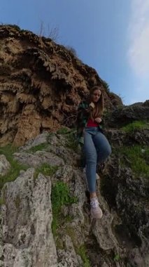 Dikey video. Uçurum Yamacında Sarp Kayalıklardan Aşağı İnen Bir Kadın, Parlak Bir Gökyüzünün Altında Okyanusa Bakan Vegetasyon Altında. Tek Kıyı Keşfi