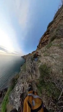 Dikey video. Rocky Cliffside 'da Dişi ve Erkek Gezgin, Kadın Ufuk' a Uzanan Okyanusla Yakın Dururken Kayadan Aşağı Tırmanan Adam. Cliffside Macerası
