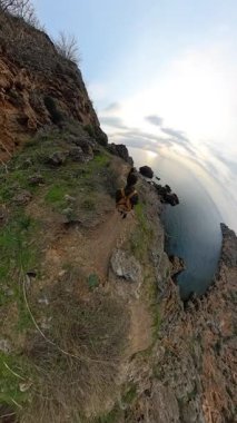 Dikey video. Bir Dar Kayalıklarda Dar Kayalık Patikada Yürüyen Erkek ve Kadın Gezgin Altında Büyük Okyanusu Gösteren Küçük Bir Gezegen Efektiyle Yakalandı. Sahne Kıyı Yolculuğu