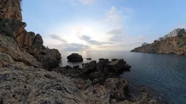 Panorama Bir Erkek ve Kadın Gezgin Okyanus kenarındaki Jagged Kayalıklarda Otururken, Kayalıklar Uzağa Uzanıyor ve Sakin Su Bulutlu Gökyüzünü Yansıtıyor. Sahne Kıyı Dinlenme