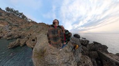Gün batımında okyanusa bakan Rocky Cliffs 'in üzerinde dikilen bir çift, Manzaranın tadını çıkarırken kadının erkeğe karşı sevgiyle eğilmesiyle. Romantik Kıyı Anı