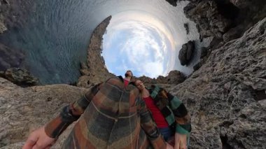 Uçsuz bucaksız ufku ve engebeli kayaları gösteren küçük bir gezegen perspektifi tarafından çevrelenmiş Uçurum kenarında öpüşen bir çift. Sahil Sahil Sahnesi