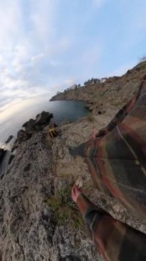 Dikey video. Okyanusa Bakan Uçurumlarda Duran Bir Adam Bir Sırt Çantası Alırken Bir POV Bakış Alanından Çekildi. Engebeli Kıyı Anı