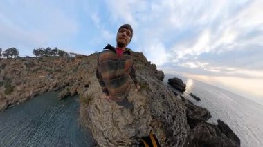 Okyanus kıyısındaki Jagged Rocks 'ta Sırt Sırtında Yürüyen Bir Adam, Yukarı Kaldırıyor ve Omuzlarına Koyuyor, Üçüncü Perspektiften Çekiyor. Engebeli Kıyı Sahnesi