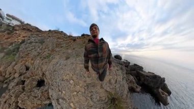 Kafası yukarı eğilmiş, Jagged Kayalar ve Arka planda Okyanus ile çevrili, Kayalık Kayalıklarda Duran Bir Erkek Kadın Yakın Duruyor. Sahne Kıyı Anı