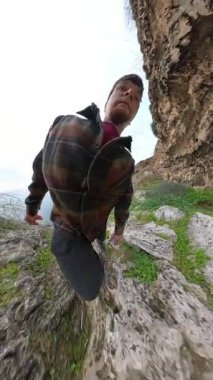 Dikey video. Ekose ceketli bir adam mağara açılışı yakınlarındaki Rocky Trail 'e tırmanıyor, çarpık küresel perspektifte yakalandı, kadın önümüzde yürüyor. Macera Yürüyüşü
