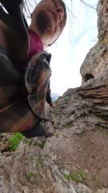 Dikey video. Bitki örtüsüyle çevrelenmiş Rocky Ledge Adam Ölçekleme Destek için ileriye uzanma, Sapkın Geniş Açı Görüş 'ten yakalanma. İleriye Tırmanan Kadın Derinlik ekler. Takım Macerası