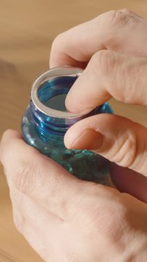 Dikey video. Şeffaf Sarı Omega-3 Softgel Kapsülleri Mavi Şişe 'den Palmiye' ye dökülen eller, Sıcak Doğal Işıkta Tahta Masa 'ya yakın çekim. Beslenme Ek ve Sağlık Konsepti