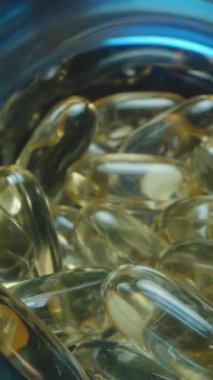 Dikey video. Görünümü Parlak Işık, Makro Perspektif ile aydınlatılmış Jelatin Balık Yağı Kapsülleriyle dolu Mavi Şeffaf Kavanoza Kapat