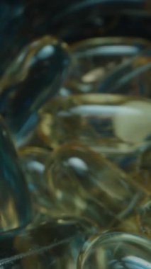 Dikey video. Altın Jelatin Kapsülleri ve Beyaz Tabletler içeren Açık Mavi Gözlerin Çeşitliliği, Mavi Vitamin Şişeleri ve Karanlık Bir Arkaplanda İlaveler