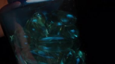 Mavi Şişenin İçindeki Altın Şeffaf Kapsüllerin Yakın Görüntüsü, Derin Işıkla Parlak Yüzeyleri ve Açıklığına Odaklandı. Günlük Beslenme