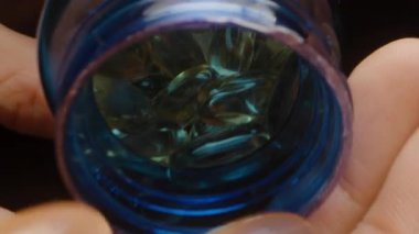 Altın Şeffaf Jelatin Kapsülleri Mavi Şişe 'den Açık El' e dökülüyor. Parlak Doku Besleyici Dolly kaydıracını vurguluyorlar..