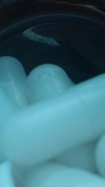 Dikey video. Beyaz Kapsüller Mavi Şişe 'den Açık El' e akıyor. Pürüzsüz Yüzeylerini ve Şekil Sağlığını ve Sağlık Bakım Dolly kaydırıcısını vurguluyorlar. Kapatın..