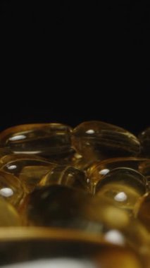 Dikey video. Omega 3 Kapsüllerinin Dolly Kaydırıcı Kapsülleri, Kamera Altın Şeffaf Dokularını Vurgularken ve Parlatıcı Bitirici Eklentileri Tamamlarken Açılırken Uzaklaşıyor