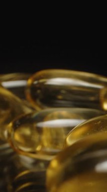 Dikey video. Altın Şeffaf Omega 3 Kapsüllerinin Dolly Kaydırıcısı Pürüzsüz Dokularını Vurguluyor ve Karanlık Arkaplan Besleyici Yansımalarına Yansıtıyor