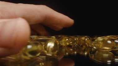 Altın Şeffaf Omega 3 Kapsülleri Parlak Bitiş ve Net Beslenme Eklentilerini Vurgulayan Yansıtıcı Yüzeye Elle Bırakılıyor