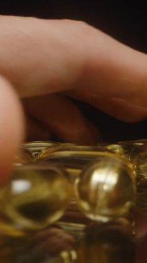 Dikey video. Altın Şeffaf Omega 3 Kapsülleri Parlak Bitiş ve Net Beslenme Eklentilerini Vurgulayan Yansıtıcı Yüzeye Elle Bırakılıyor