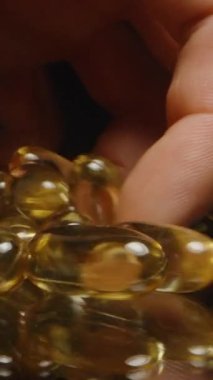 Dikey video. Pürüzsüz Doku ve Parlak Görünüm Sağlıklı Yaşam 'ı gösteren Yansıtıcı bir yüzeyden Altın Şeffaf Kapsül Seçen Parmaklar