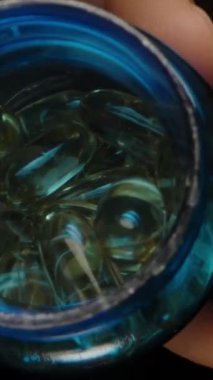 Dikey video. Omega 3 Kapsülleri Mavi Kavanozdan Hareket Eden Bir El 'e dökülüyor Parlak Altın Yüzeylerini ve Pürüzsüz Doku Sağlıklarını ve Sağlık Bakımlarını Gösteriyorlar
