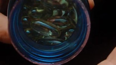 Elleri Altın Şeffaf Omega 3 Kapsülleriyle Doludur Mavi Kavanoz 'dan dökülen Parlak ve Pürüzsüz Doku Günlük Beslenme Dolly sürgüsü, yakın çekim.