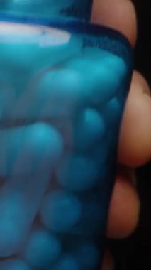 Dikey video. Beyaz Kapsüller Mavi Şişe 'den bir ele akıyor Pürüzsüz yüzeyi ve Parlak Sağlık ve Sağlık Bakımını Gösteriyorlar