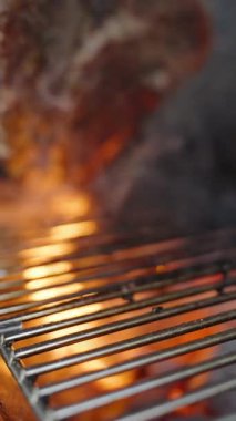 Dikey video. Yavaş çekimde, El ele tutuşan maşalar ızgaradan leziz bir bifteği kaldırarak kömürleşmiş kenarlarını yakıyor ve yüzey ızgara pişirme uzmanlığı kazanıyor.