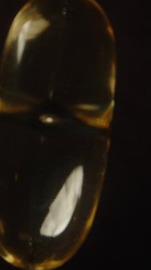 Dikey video. Genel Görünüm Altın Şeffaf Omega 3 Kapsül Dönüşü ve Düşüşü Yavaş Çekimde Parlak Dokusunu ve Yumuşak Yüzey Besleyici Eklemesini Vurguluyor