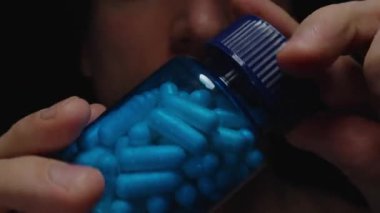 Beyaz ve Mavi Kapsüllerle Dolu Açık Mavi Şişe Bir Adamın Önünde, Hapların Dokusunu ve Parlak Sağlık Özelliklerini Vurguluyor