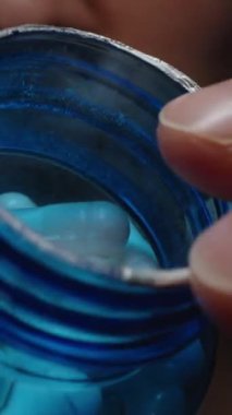 Dikey video. Açık Mavi Şişe 'den Beyaz Kapsül Seçen Bir Adam Pürüzsüz Yüzeyi ve Besleyici İlacın Hassas Şeklini Gösteriyor