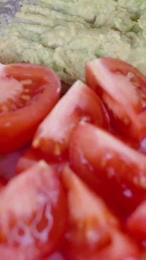 Dikey video. Bir tabak Dilimlenmiş Domates Dilimlenmiş Avokado, Servise Hazır, Parlak Kırmızı ve Yeşil Renkler, Yakın plan