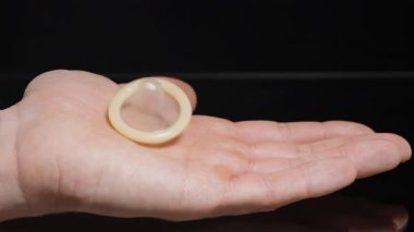 Açık El 'e Düşen Kondom ve Yavaş Çekimde Yavaş Çekimde Sıkıştırılmak Cilt Dokusuna ve Kondomun Yumuşak Malzemesine Vurgu Yaparak Güvenli Seçim ve Sorumluluğu Temsil Ederek