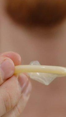Dikey video. Latex Dokusuna Odaklı Bir Kondom Yakın Çekim, Arka planda Bir Erkek figürü, Bulanık, İyi-Aydınlatma Ortamı