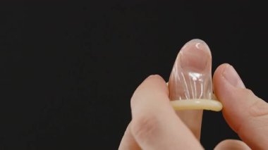 Siyah bir zemin karşısında parmağına prezervatif takan bir adam, Doğru Tekniği ve Kullanımı Ellere ve Kondoma Odaklı Gösteriyor