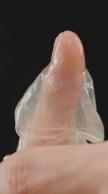 Dikey video. Siyah bir zemin karşısında parmağından prezervatifi çıkaran, elleri ve prezervatifi odaklı uygun tutma ve imha tekniklerini gösteren bir adam.