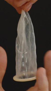 Dikey video. Siyah Arkaplan Karşısında Bir Parmağın Üzerinde Kondom Açan Eller, Dikkatli Tutma Odaklı Uygun Uygulama Tekniğini Gösterme Teknikleri