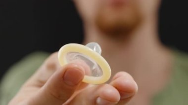 Kameranın önünde, Siyah Arkaplan Karşısındaki Dairesel Şekil 'i net bir şekilde gören bir adam prezervatif gösteriyor.