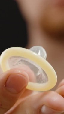 Dikey video. Kameranın önünde, Siyah Arkaplan Karşısındaki Dairesel Şekil 'i net bir şekilde gören bir adam prezervatif gösteriyor.