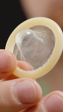 Dikey video. Siyah Arkaplan Karşısında Kameraya Yakın Kondom Tutan Bir Adam Tasarım ve Fonksiyonunu Vurguluyor