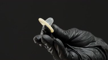 Siyah Eldivenli Bir El Parmaklar Arasında Bir Kondom Çimdikliyor, Uygun Tutuş ve Güvenliği Vurguluyor