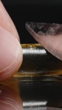 Dikey video. Bir Omega-3 balık yağı kapsülünü kesen bıçağın yakın plan çekimi, sıvıyı serbest bırakır, parmakları yansıtıcı yüzeyde sabit tutar, hassasiyet ve jel dokusunu gösterir..