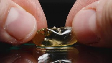 Parmakların yansıtıcı yüzeyde saydam bir Omega-3 balık yağı kapsülünü sıkıştırması, sıvı ve kabarcıklar oluşması, dokunun ve parlak detayların yakından incelenmesi.