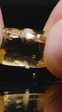 Dikey video. Saydam bir Omega-3 balık yağı kapsülünü sıkıştıran parmaklar, içinde kabarcıklar oluşmasına ve sıvının ortaya çıkmasına neden oluyor..