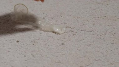 Açık renkli bir halıdan sarılmış bir prezervatifi kapan, yakından gören, objeyi tutan parmaklara odaklanan, halı dokusu açıkça görülebilen bir el..