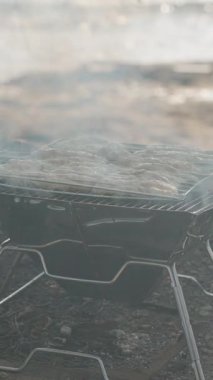 Dikey video. Alevler yoğunlaştıkça, Arkaplanda Sahilde ve Denizde Yanmayı Önlemek İçin Izgaranın Üzerinde Bir Et Rafı Yükseltmek
